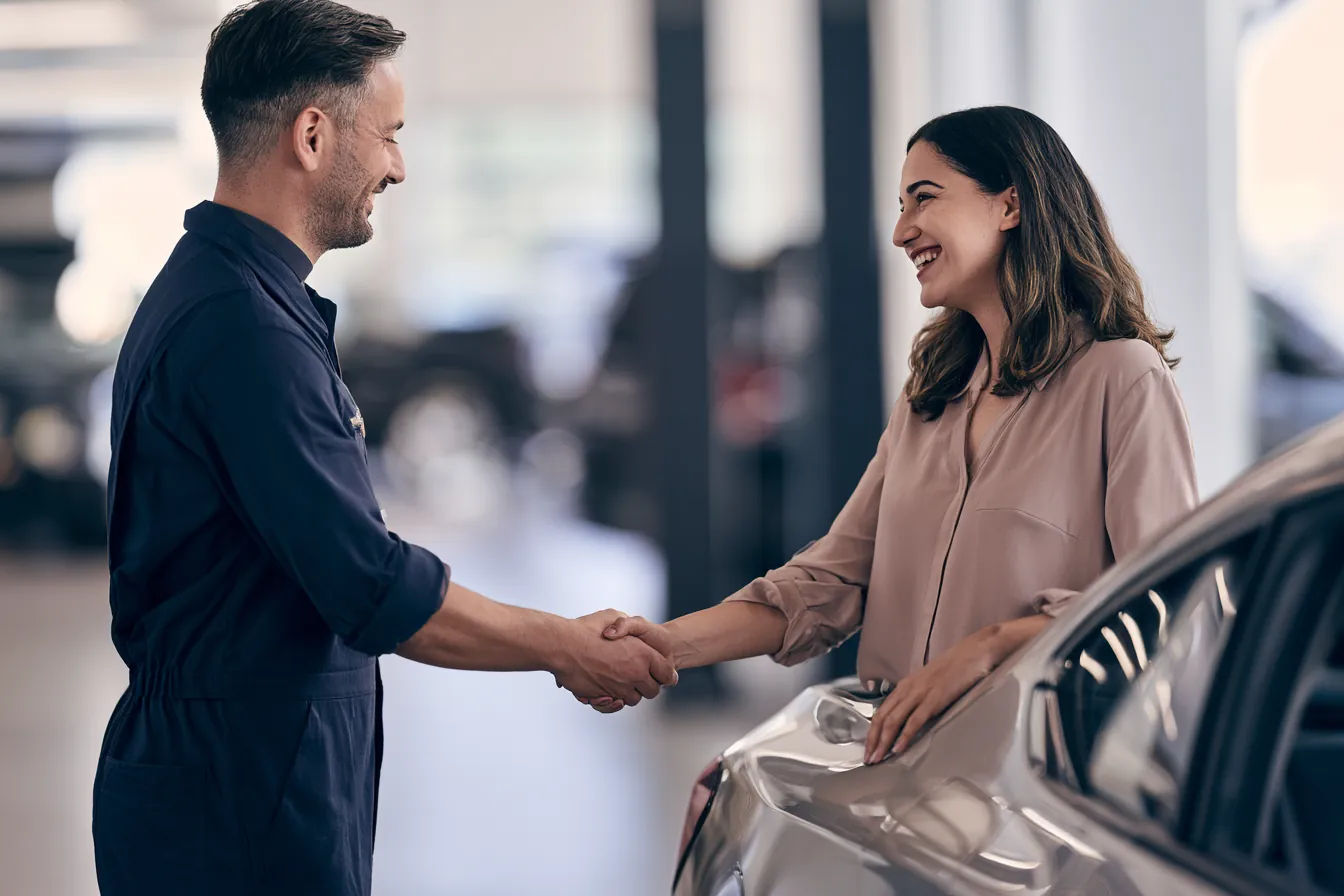 Mechanic shaking hands with a customer beside a repaired sedan in a bright garage