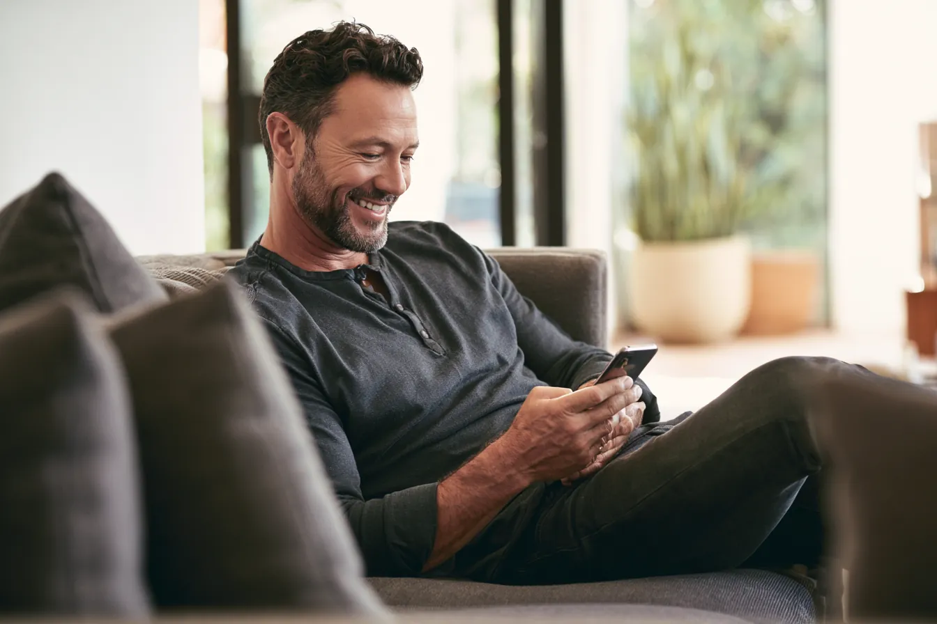 Man relaxing on a sofa reviewing a personal loan offer on his phone